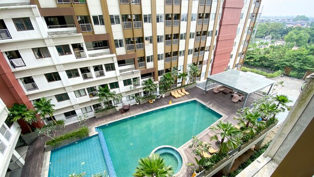A rooftop swimming pool with a wooden deck, surrounded by palm trees and a view of a cityscape. - Great Choice Studio Apartment LRT City Jatibening (Bekasi)