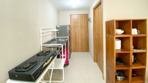 A compact kitchen with a gas stove, a sink, a refrigerator, and a wooden cabinet with shelves. - Great Choice Studio Apartment LRT City Jatibening (Bekasi)