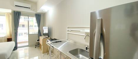 Habitación de hotel con cama, escritorio, refrigerador, lavamanos y ventana con cortinas.