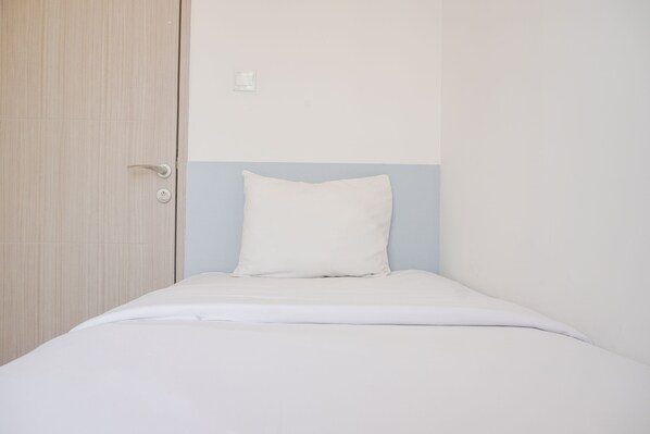 A small, single-bed room with a wooden wardrobe, a white bed, and a light blue accent wall.