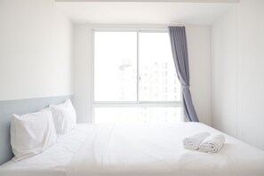 A hotel room with a bed, pillows, and a window with curtains.
