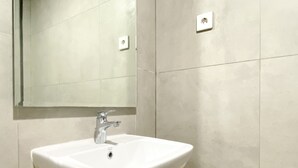 Une salle de bain avec un lavabo blanc, un miroir et un interrupteur sur le mur.