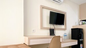 Une chambre moderne dotée d’un téléviseur à écran plat fixé au mur, d’une petite kitchenette équipée d’un réfrigérateur et d’une machine à café, et d’un canapé capitonné.