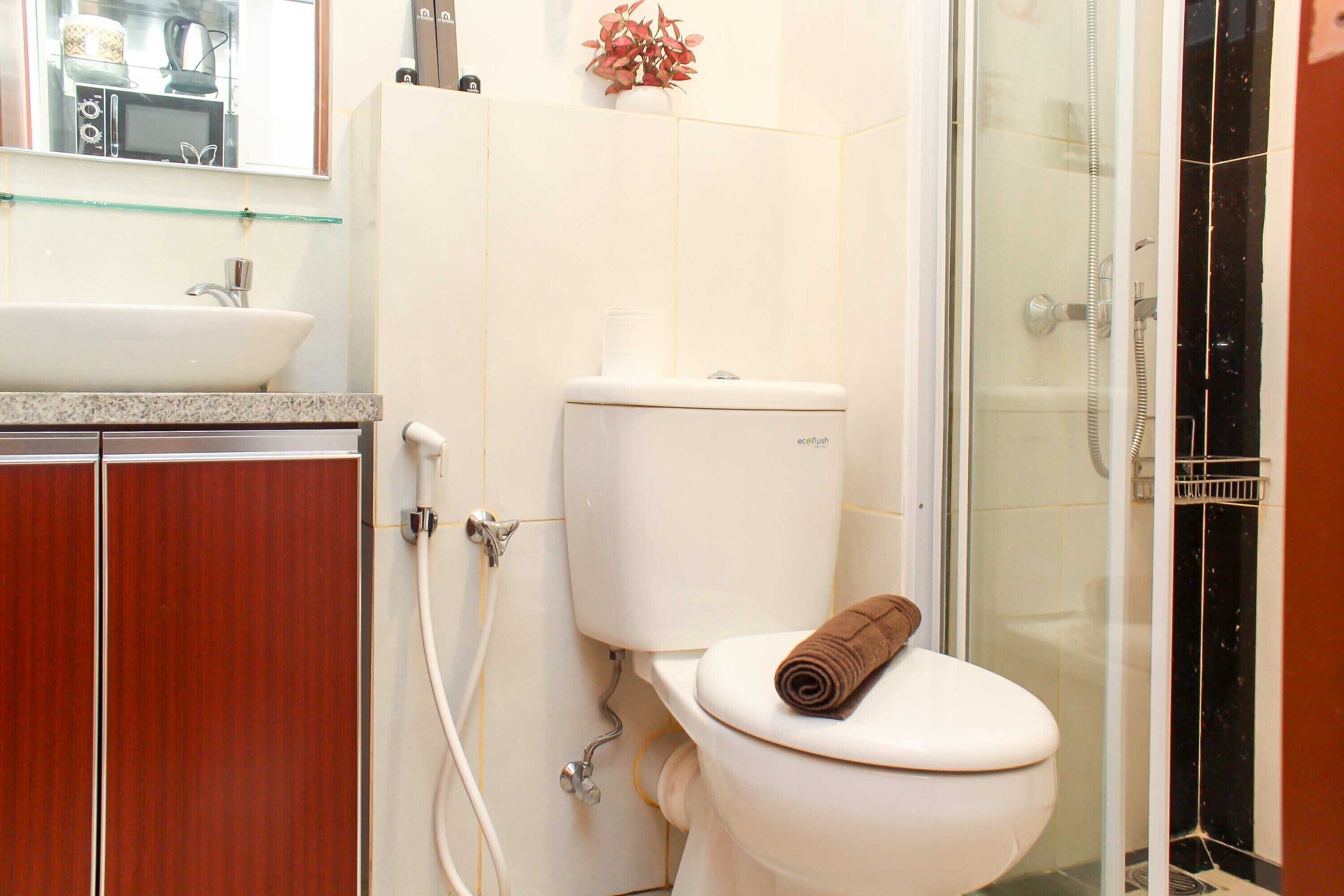 A bathroom with a white toilet, a glass shower enclosure, and a wooden cabinet.
