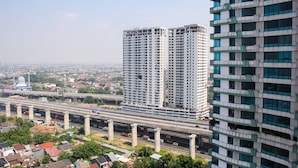 A high-rise building with multiple floors, surrounded by a cityscape and a highway. - Comfort Living Studio Apartment At Grand Kamala Lagoon Near Shopping Center (Bekasi)