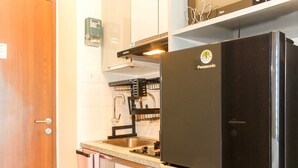 A compact kitchen with a black refrigerator, a stainless steel sink, and a dish rack. - Comfort Living Studio Apartment At Grand Kamala Lagoon Near Shopping Center (Bekasi)