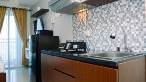 A modern kitchen with a black countertop, a stainless steel sink, and a tiled backsplash. - Modern And Comfy Studio At Grand Dhika City Apartment (Bekasi)