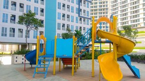 A playground with slides and climbing structures, surrounded by a building with multiple windows and balconies. - Modern And Comfy Studio At Grand Dhika City Apartment (Bekasi)