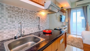 A modern kitchen with a double sink, a red induction cooktop, and wooden cabinets. - Homey And Relaxing Studio Grand Dhika City Apartment (Bekasi)