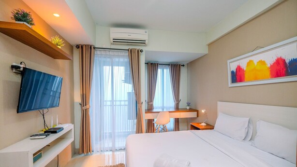 A hotel room with a bed, a TV, a desk, and a painting. - Homey And Relaxing Studio Grand Dhika City Apartment (Bekasi)
