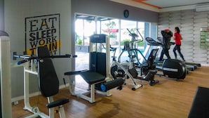 A gym with various exercise equipment, a motivational poster, and a clock on the wall. - Homey And Relaxing Studio Grand Dhika City Apartment (Bekasi)