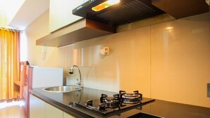 A modern kitchen with a gas stove, stainless steel sink, and a black countertop. - Fabulous Studio Grand Dhika City Apartment (Bekasi)