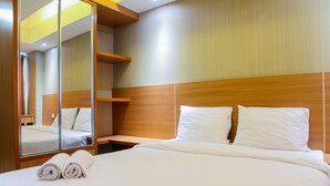 A hotel room with a large bed, a wooden headboard, a bedside table, and a mirror. - Fabulous Studio Grand Dhika City Apartment (Bekasi)