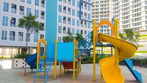 A playground with slides and climbing structures, surrounded by a building with multiple windows and balconies. - Fabulous Studio Grand Dhika City Apartment (Bekasi)