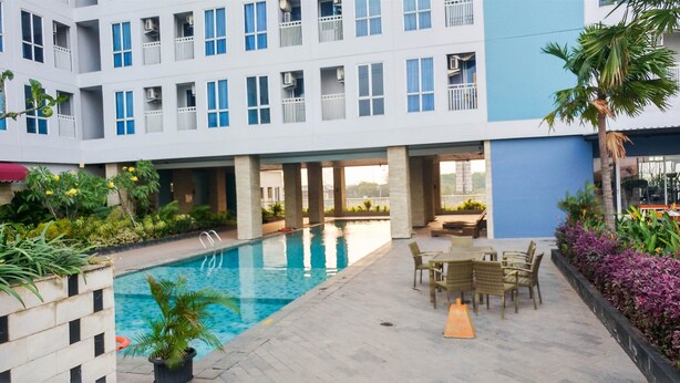 A hotel courtyard with a swimming pool, outdoor seating, and lush landscaping. - Comfortable Studio Apartment Grand Dhika City (Bekasi)
