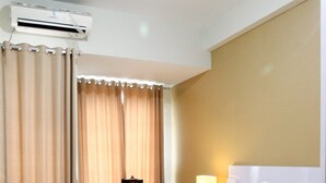 A hotel room with a bed, desk, chair, and an air conditioning unit. - Comfortable Studio Apartment Grand Dhika City (Bekasi)