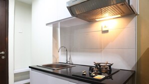 A compact kitchen with a black countertop, stainless steel sink, and a stove. - Comfortable Studio Apartment Grand Dhika City (Bekasi)