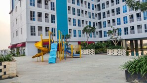 A playground with slides and climbing structures in front of a multi-story building with balconies. - Comfortable Studio Apartment Grand Dhika City (Bekasi)