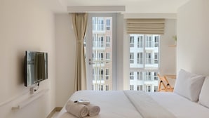 A hotel room with a bed, a TV mounted on the wall, a window with curtains, and a view of the building outside. - Best Deal Studio Tokyo Riverside Pik 2 Apartment (Teluknaga)