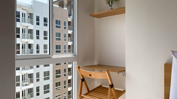 A room with a wooden chair, a small wooden shelf, and a window with a view of a building. - Best Deal Studio Tokyo Riverside Pik 2 Apartment (Teluknaga)