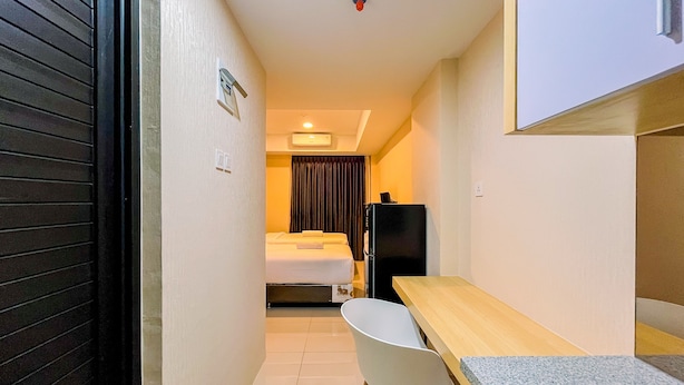 Habitación de hotel pequeña con cama, escritorio, silla, refrigerador y un lavamanos.