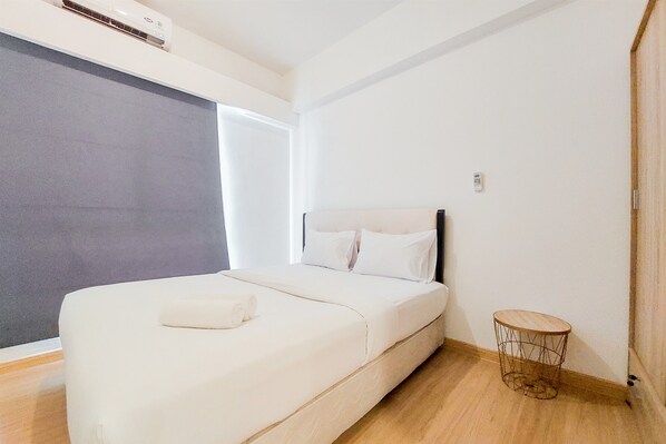 Simple, functional space with a single bed, side table, and stool.