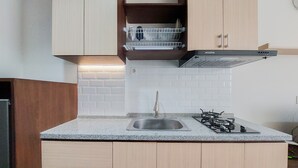 A kitchen with a granite countertop, stainless steel sink, and a gas stove. There are wooden cabinets and a dish rack above the sink. - Homey Studio At Bintaro Icon Apartment (South Tangerang)