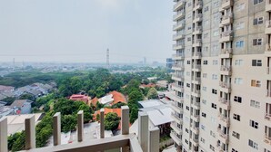 A high-rise building with multiple balconies and a view of a residential area with houses and greenery. - Homey Studio At Bintaro Icon Apartment (South Tangerang)