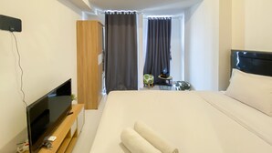 Een moderne hotelkamer met een groot bed, een flatscreen televisie op een houten standaard, een klein tafeltje met een plant en uitzicht buiten door een raam met gordijnen.