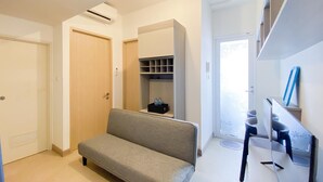 Quarto moderno com sofá cinza, porta de madeira, prateleira embutida e pequena mesa com uma garrafa de água.