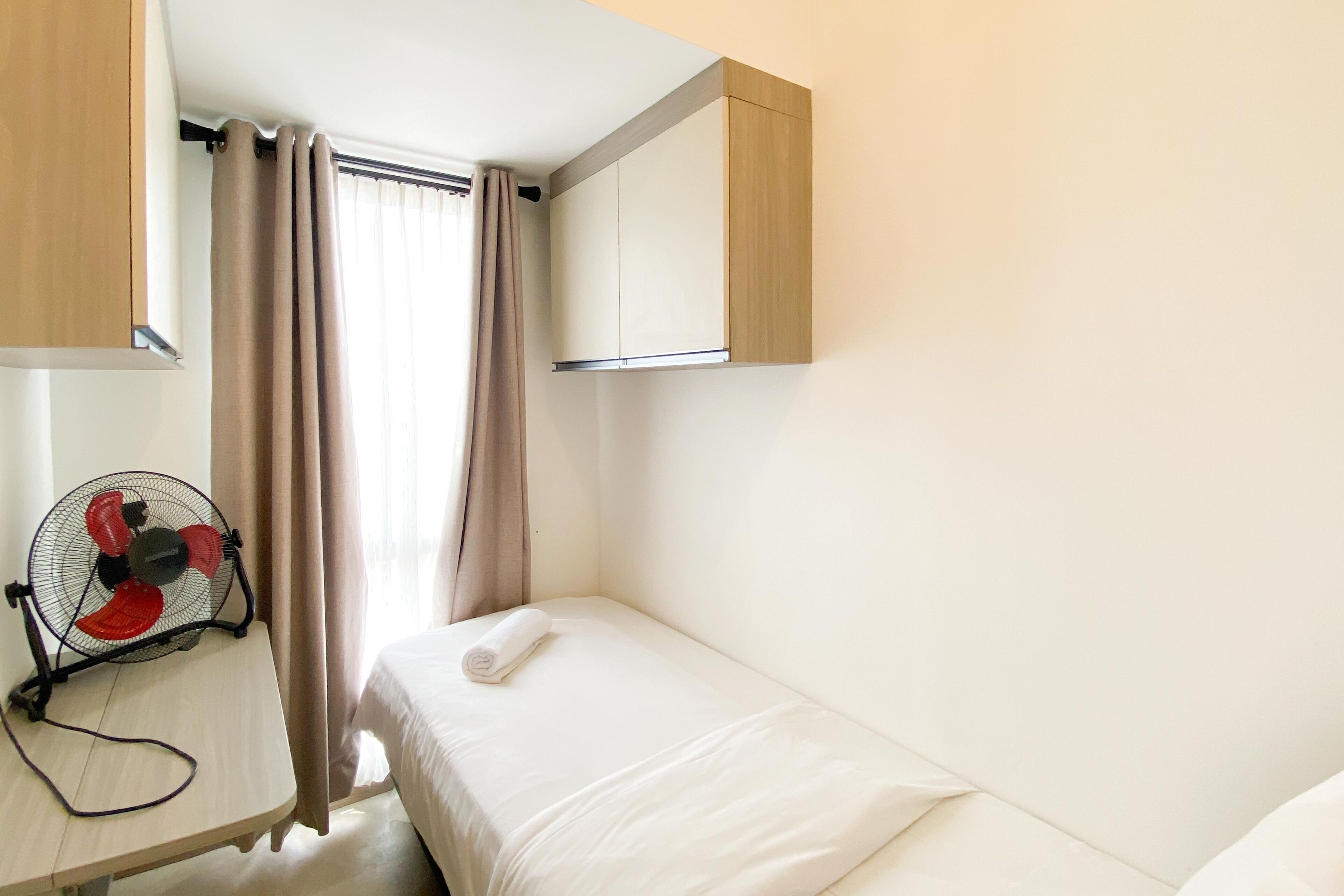 A hotel room with a bed, a desk with a fan, and a wardrobe.