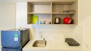 Uma cozinha compacta com geladeira embutida, pia e prateleiras acima contendo utensílios de cozinha e chaleira.