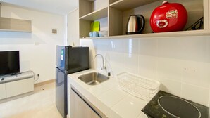 Uma cozinha moderna com azulejos brancos, uma pia de aço inoxidável, uma geladeira preta, uma chaleira vermelha e um fogão por indução preto.