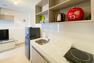 A modern kitchen with white tiles, a stainless steel sink, a black refrigerator, a red kettle, and a black induction cooktop.