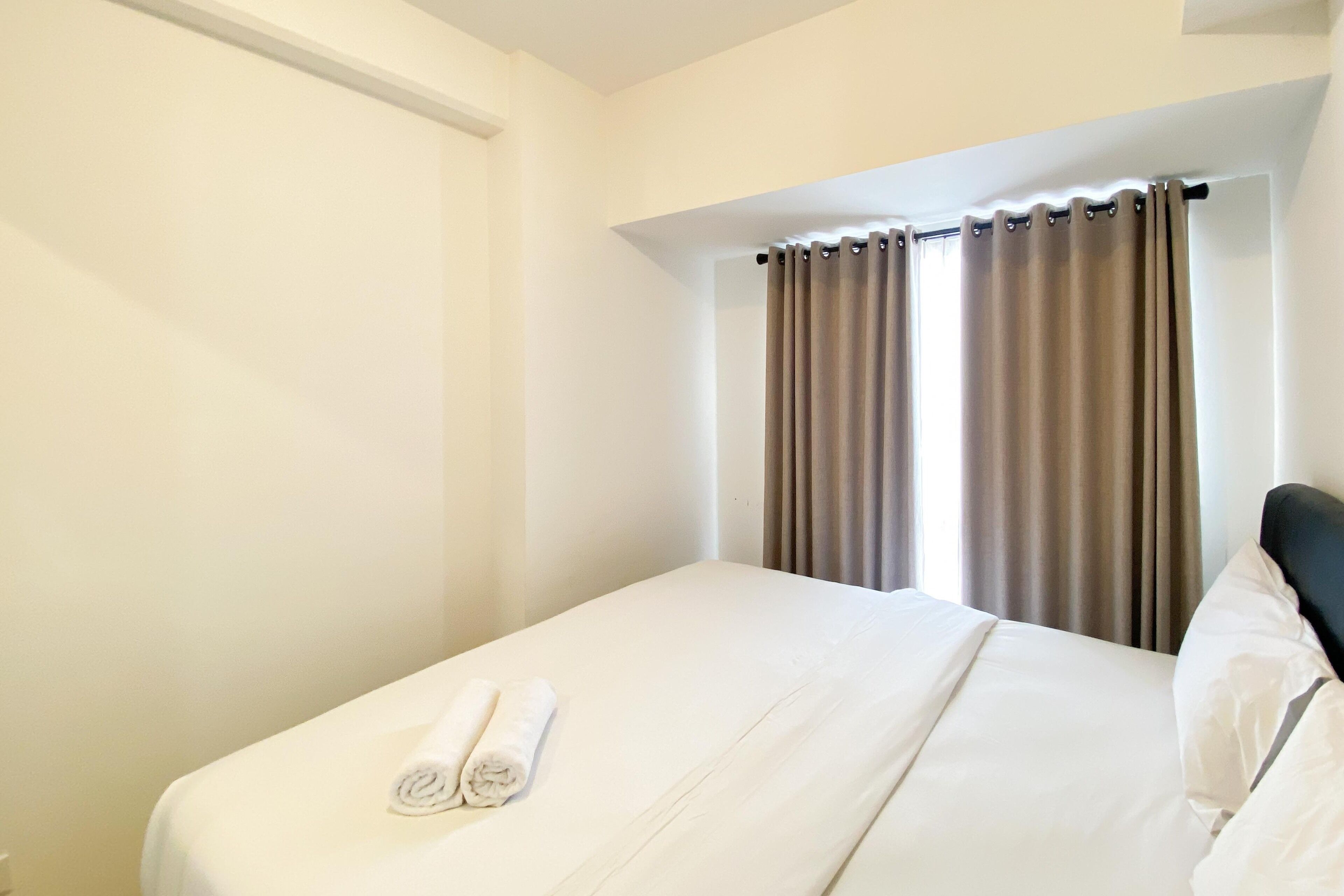 A neatly made bed with a white comforter and two rolled towels.