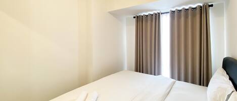 A neatly made bed with a white comforter and two rolled towels.