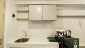 A compact kitchen with a stainless steel sink, a built-in microwave, and a coffee maker on the countertop. - Cozy Studio Tokyo Rivervide Pik 2 Apartment (Teluknaga)