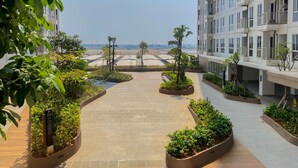 A modern residential building with a central courtyard featuring planters and a paved walkway. - Cozy Studio Tokyo Rivervide Pik 2 Apartment (Teluknaga)