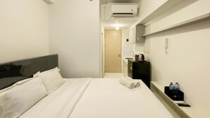 A hotel room with a bed, a bedside table with a remote control, a water bottle, and a phone. - Cozy Studio Tokyo Rivervide Pik 2 Apartment (Teluknaga)