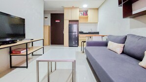 Ein Wohnzimmer mit einer Couch, einem Fernseher, einem kleinen Tisch und einer Küchenzeile im Hintergrund.