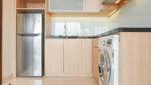 A compact kitchen with a stainless steel refrigerator, a washing machine, and wooden cabinets.