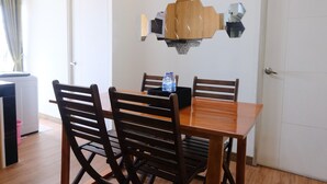 A dining area with a wooden table and four chairs, a water bottle on the table, and a door in the background. - Spacious And Modern 3Br Apartment At Gateway Ahmad Yani Cicadas (Bandung)