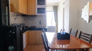 A compact kitchen with wooden cabinets, a black refrigerator, a microwave, and a dining table with chairs. - Spacious And Modern 3Br Apartment At Gateway Ahmad Yani Cicadas (Bandung)