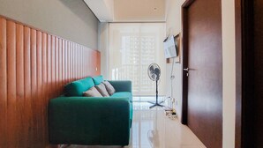 A modern living room with a green sofa, wooden panel wall, and a large window. - Comfortable And Warm 2Br Parkland Avenue Apartment (South Tangerang)