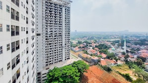 A high-rise building with multiple balconies and a view of a residential area with houses and a mosque. - Comfortable And Warm 2Br Parkland Avenue Apartment (South Tangerang)