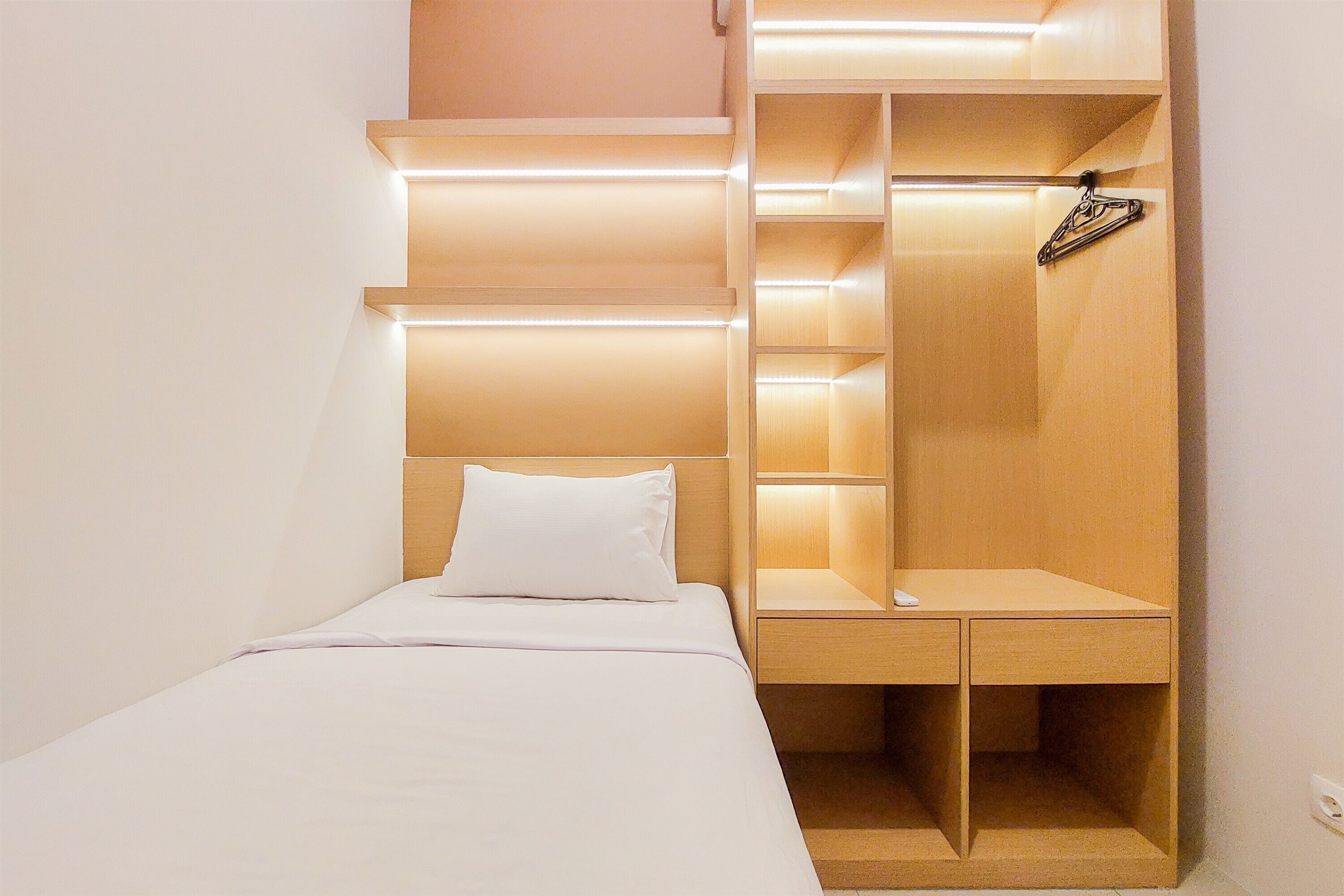Une chambre d’hôtel de taille réduite, comprenant un lit, une table de chevet en bois et des étagères intégrées.