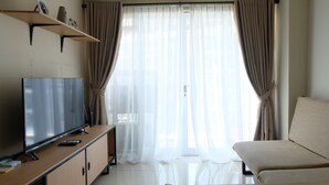 Une pièce avec un téléviseur posé sur un meuble en bois, un canapé et une fenêtre ornée de rideaux légers.