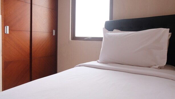 A hotel room with a bed, a window, and a wooden wardrobe.