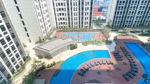 A high-rise building with a swimming pool, a basketball court, and a landscaped area with seating. - Homey And Cozy Stay Studio Room Pollux Chadstone Apartment (Cikarang)