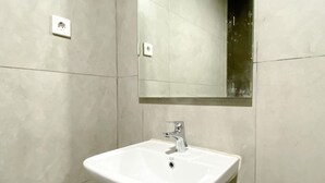 A bathroom with a white sink, a mirror, and two light switches on the wall. - Homey And Cozy Stay Studio Room Pollux Chadstone Apartment (Cikarang)